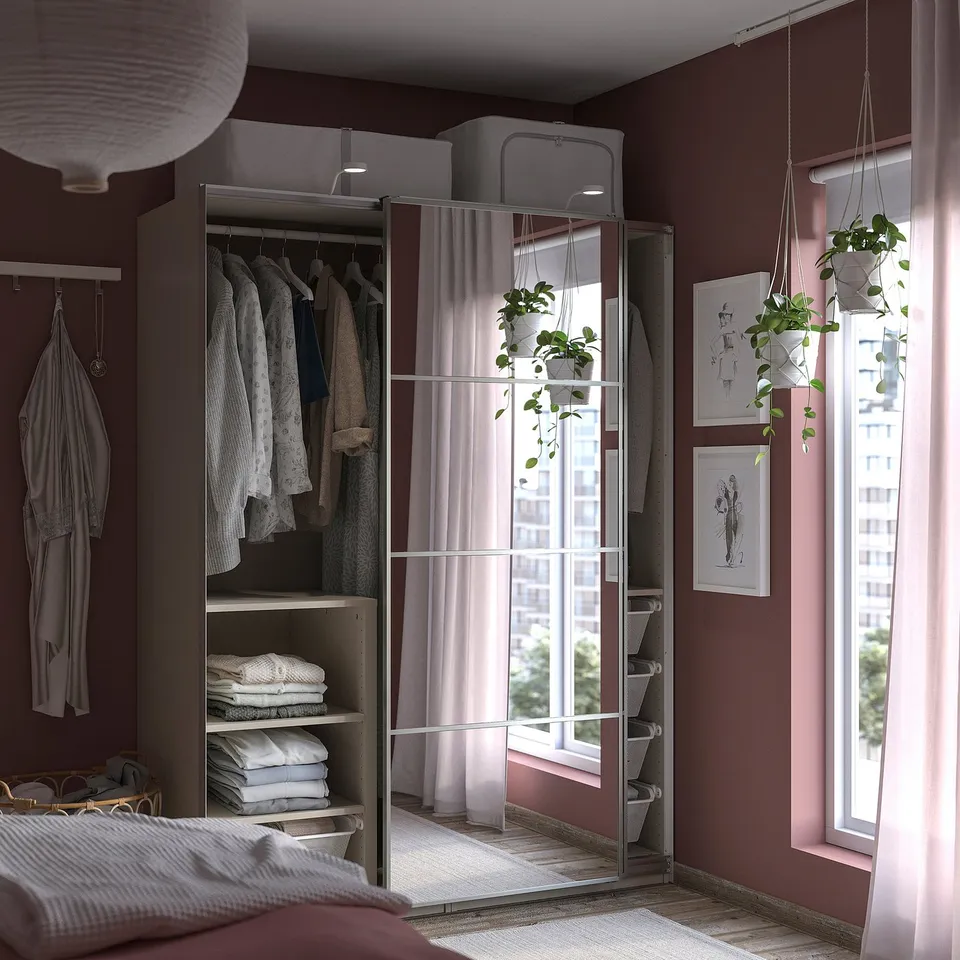 Modern bedroom with white PAX wardrobe, mirrored doors, plants, art, large window.