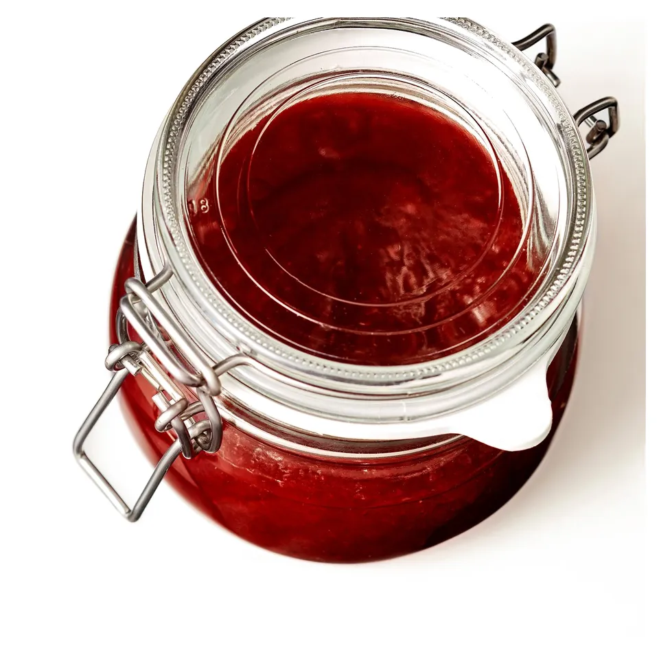 A glass jar with a metal clasp, filled with red jam, sealed airtight.