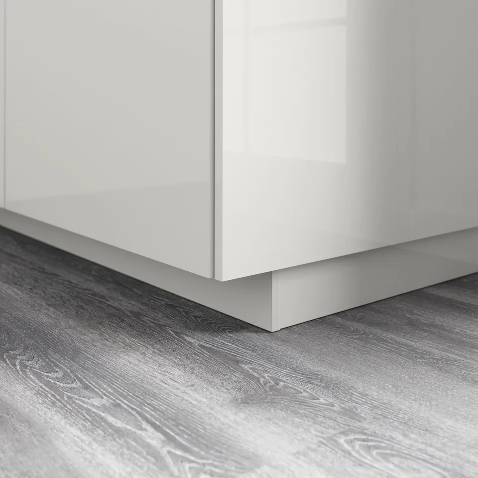 A glossy white cabinet base with grey wooden flooring. The cabinets sleek design repels moisture and dirt, ensuring a clean and modern look.