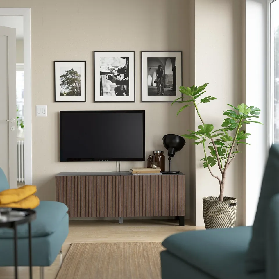 Modern living area with BESTÅ tv bench, tv, photos, green plant, turquoise chair, yellow blanket.