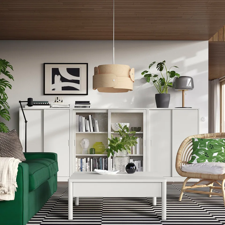 Modern living room with green sofa, patterned rug, off-white TONSTAD cabinet, wood ceiling, pendant lamp, plants, and vibrant decorative items.