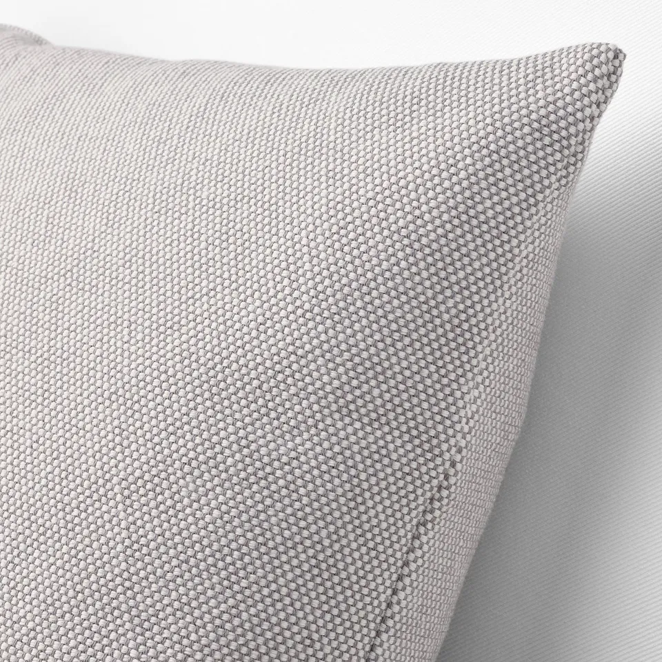 Close-up of textured, grey-white cushion on a chair, showing its intricate, knitted fabric and plump, feather-filled design.