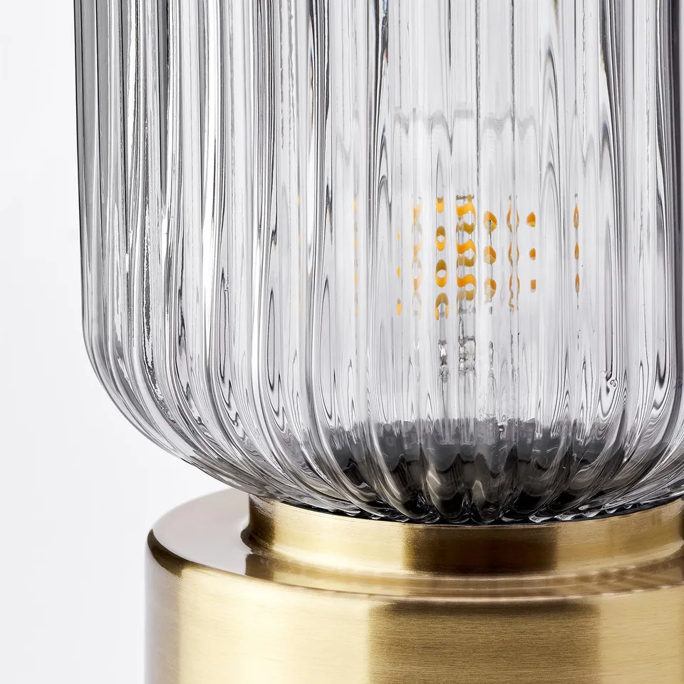 Elegant lamp with ribbed glass shade, golden base, emitting warm light.