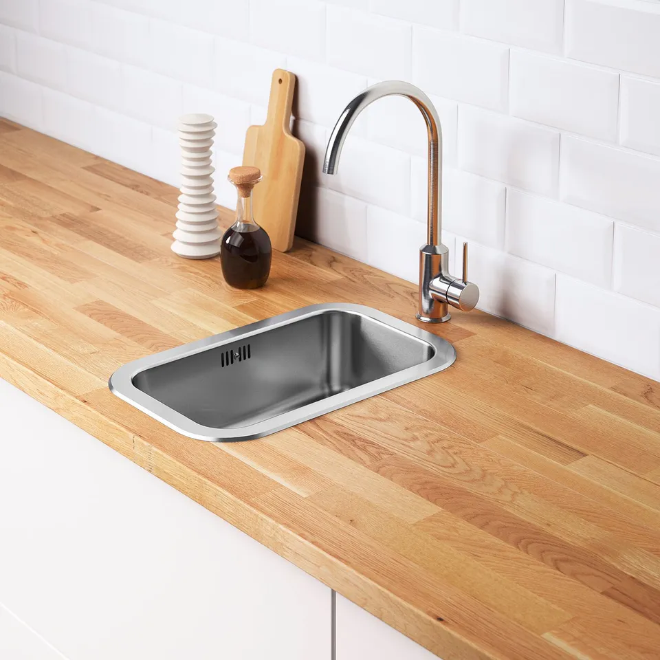 Stainless steel sink with modern tap on wooden countertop, including water trap and strainer.