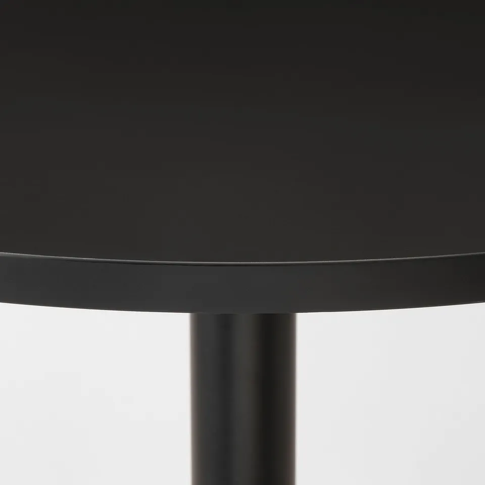 Close-up of a sleek, black round tabletop supported by a sturdy metal leg.