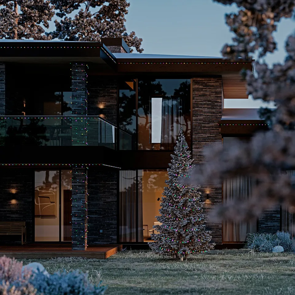 Modern home with large windows decorated with GETKÅL multicolor string lights. Tree in front, illuminated at dusk. Dark sky, trees framing the scene.