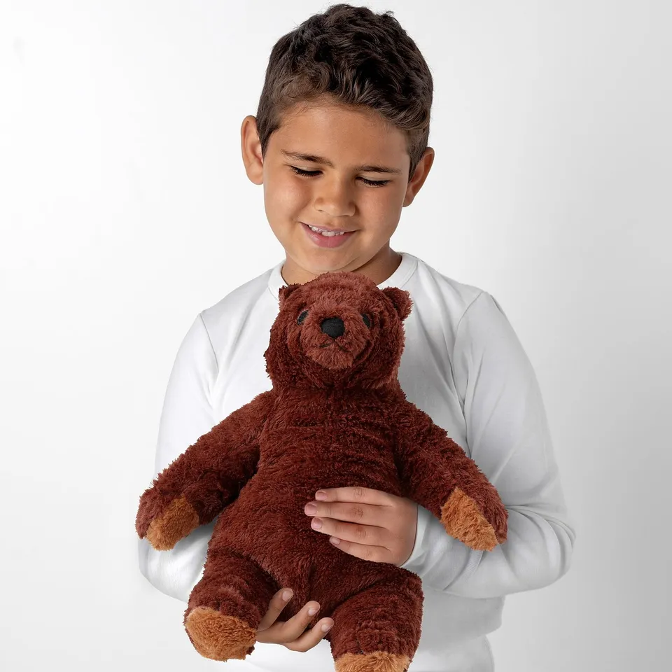 In a smiling child holds a soft, huggable teddy bear. The bear is brown, perfect for cuddling.
