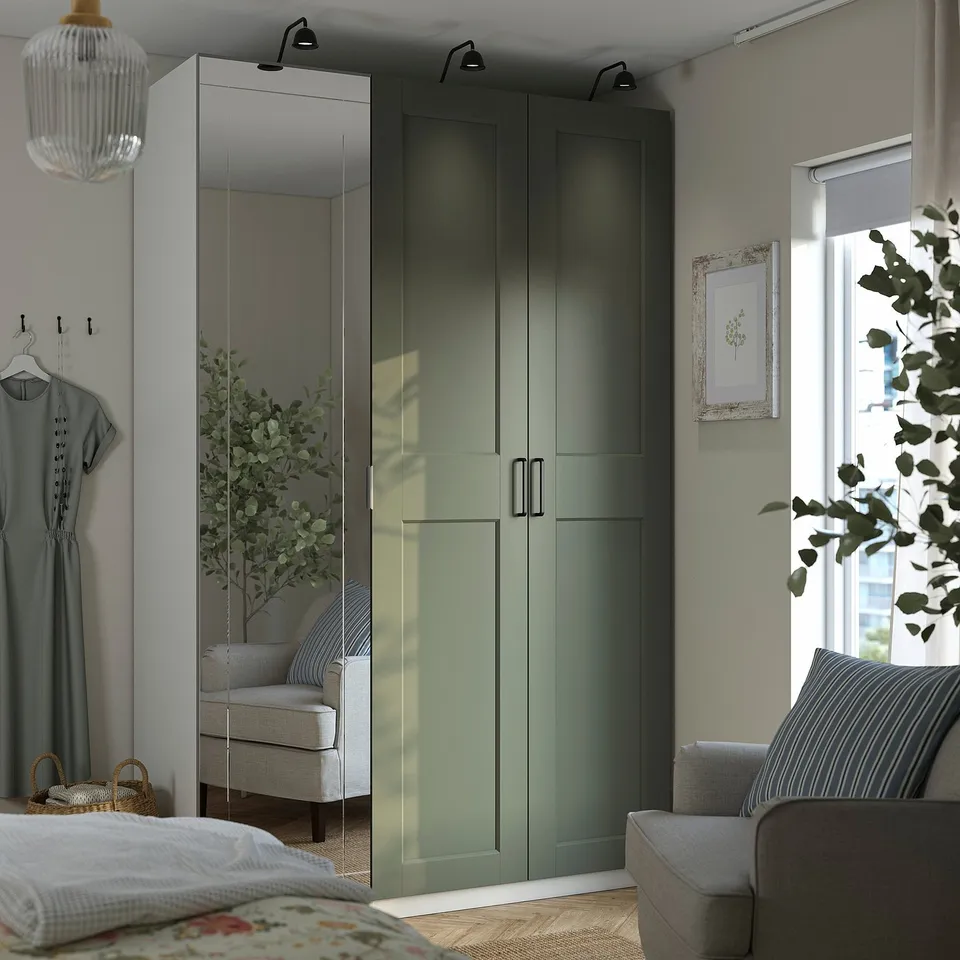 Modern bedroom with tall green PAX wardrobe, mirrored doors, grey chair, cosy bed, and bright natural light.
