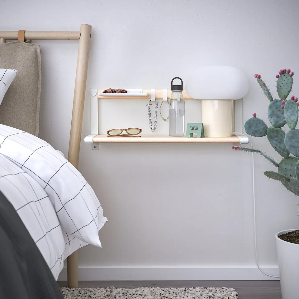 SKOMAKARE wall shelf in light wood holds glasses, keys, & bottle. Mounted beside bed with cactus plants and hooks. Minimalistic and functional.