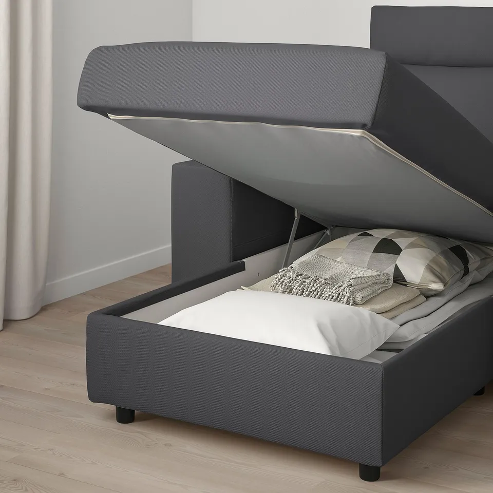 Grey fabric sofa with storage accessed by lifting seat, pillows inside.