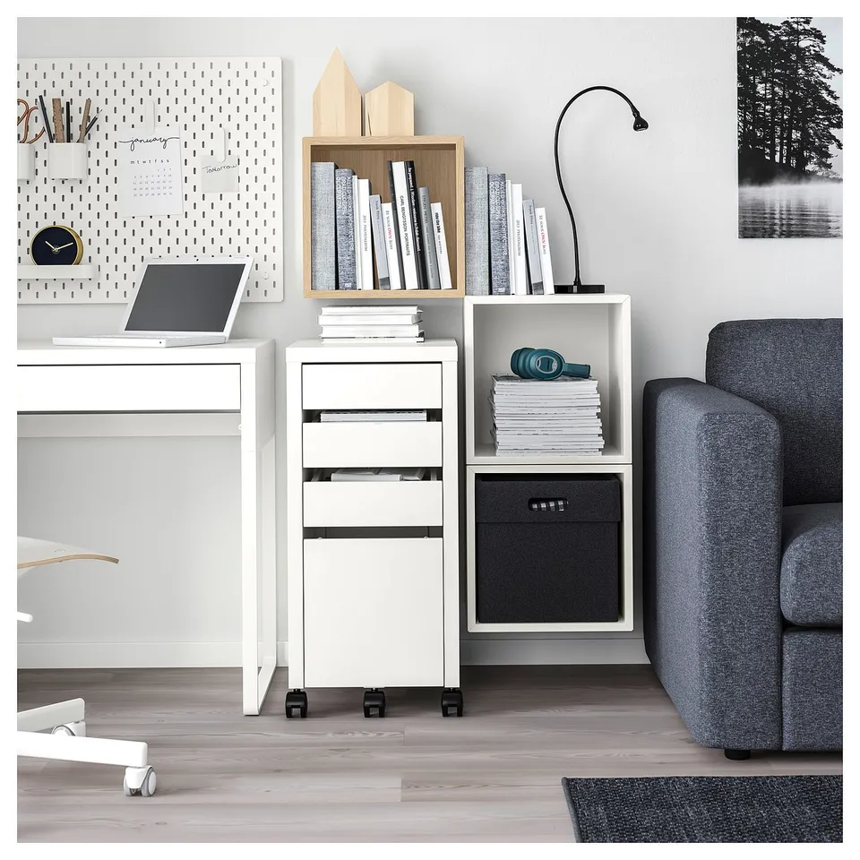 Modern home office with white EKET storage units, holding books and laptop. Grey couch and rug, wooden floor.