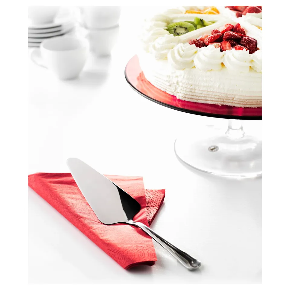 A cake on a stand with strawberries, kiwi, and a cake slicer on a red napkin.