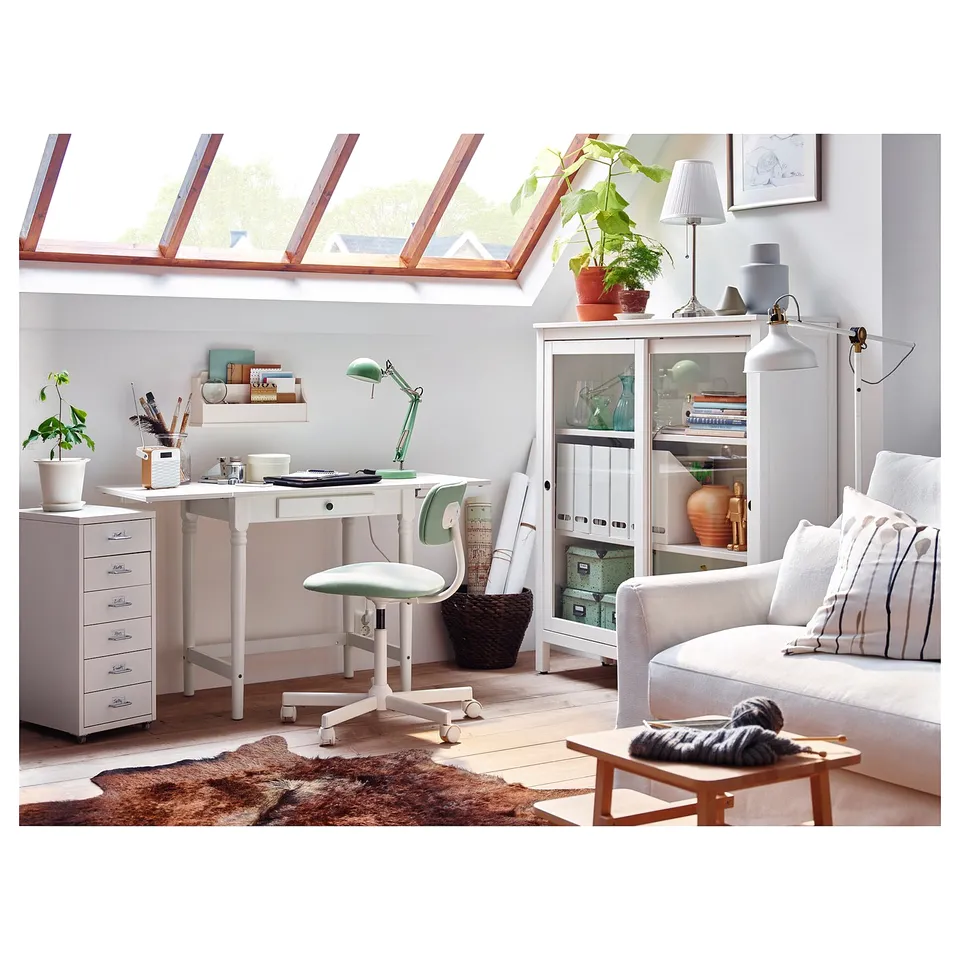 Bright, cosy room with white furniture: desk, chair, cabinet, couch. Large windows, plants, rug.
