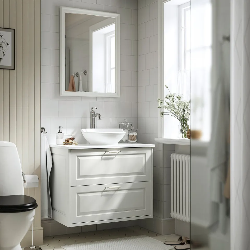 TÄNNFORSEN vanity with sink, mirror, radiator, and vase of flowers.