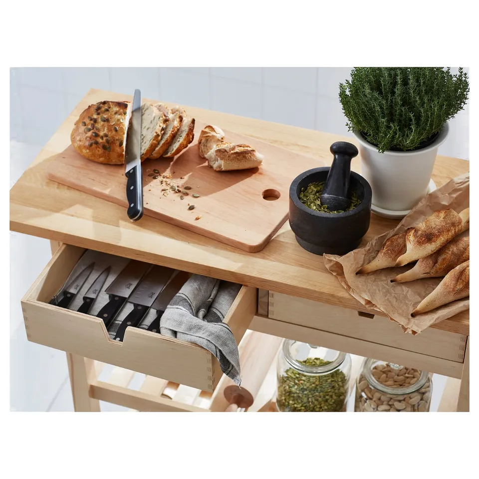Wooden kitchen cart with knife drawer and cutting board on top beside a mortar.