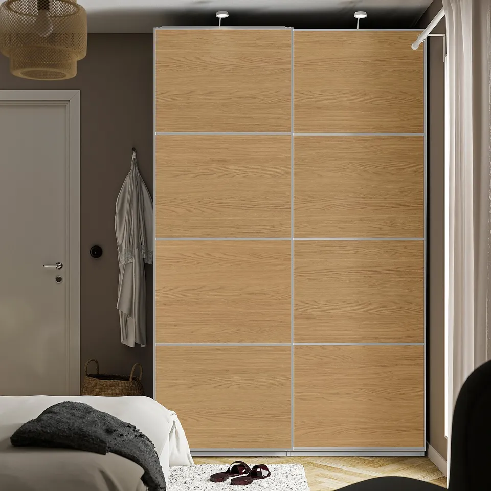 Wooden MEHAMN closet door in grey bedroom, spanning wall with clothes.