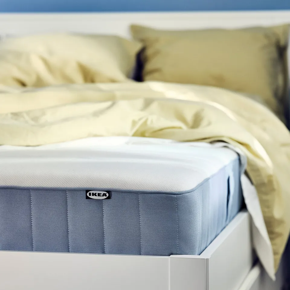 Bed with light blue IKEA VESTERÖY mattress, creamy bedding, and white frame.
