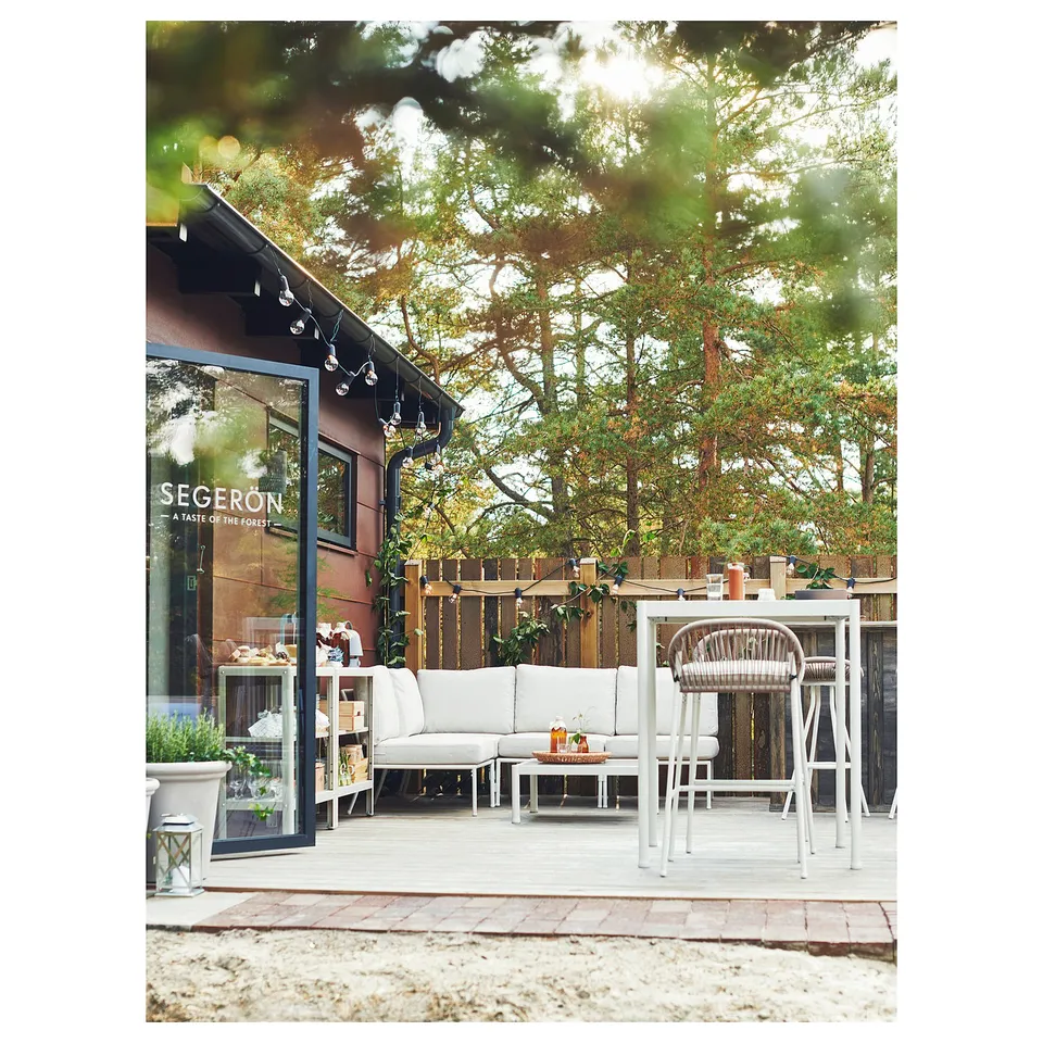 Modern outdoor patio with white SEGERÖN furniture, including sectional sofa and dining set. Surrounded by trees and wooden fencing.