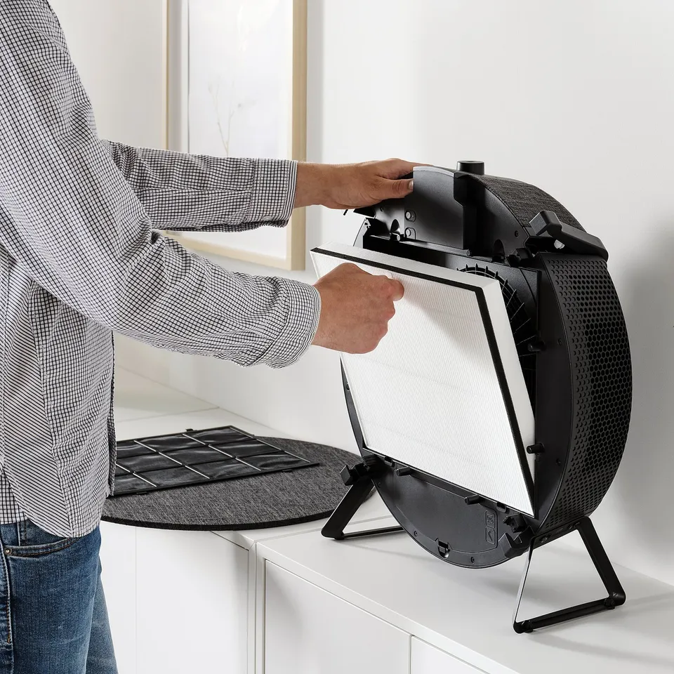 A person instals a philtre into a modern air purifier on a kitchen counter. It helps remove pollutants and odours.