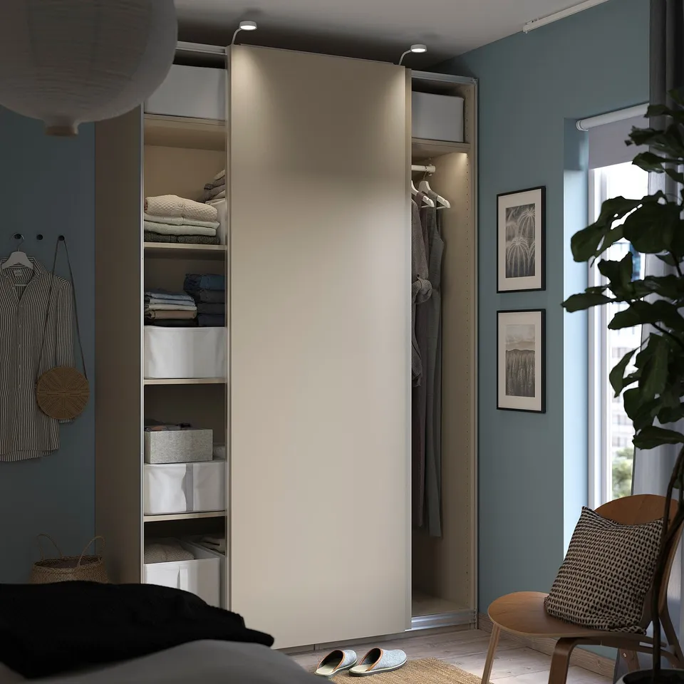 Modern bedroom with open PAX wardrobe in beige. Folded clothes, boxes, hangers, and sliding door.