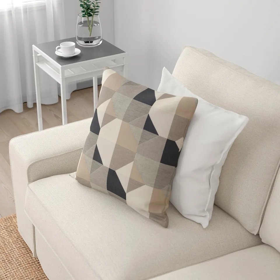 Beige sofa with patterned and white pillows, beside small table with cup and plant.