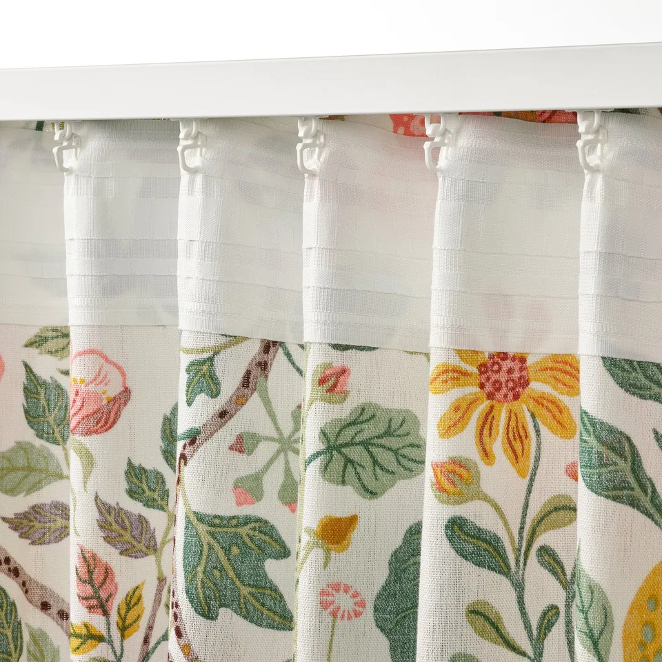 Floral curtains with heading tape hang above a window. The hooks are visible at the top, showing how theyre used to create pleats.