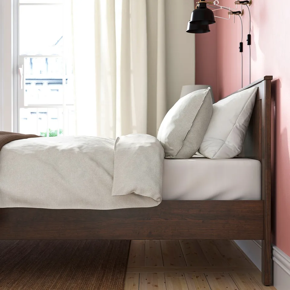 Bed with wooden frame, evenly folded white bedding, pillows, window with curtains.