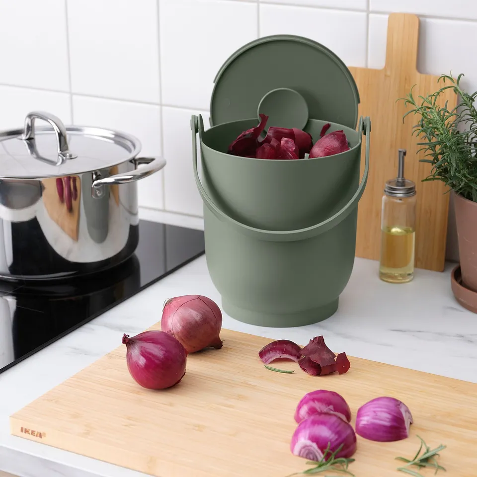 Green compost bin on counter with onions; used for kitchen waste, easy to clean.