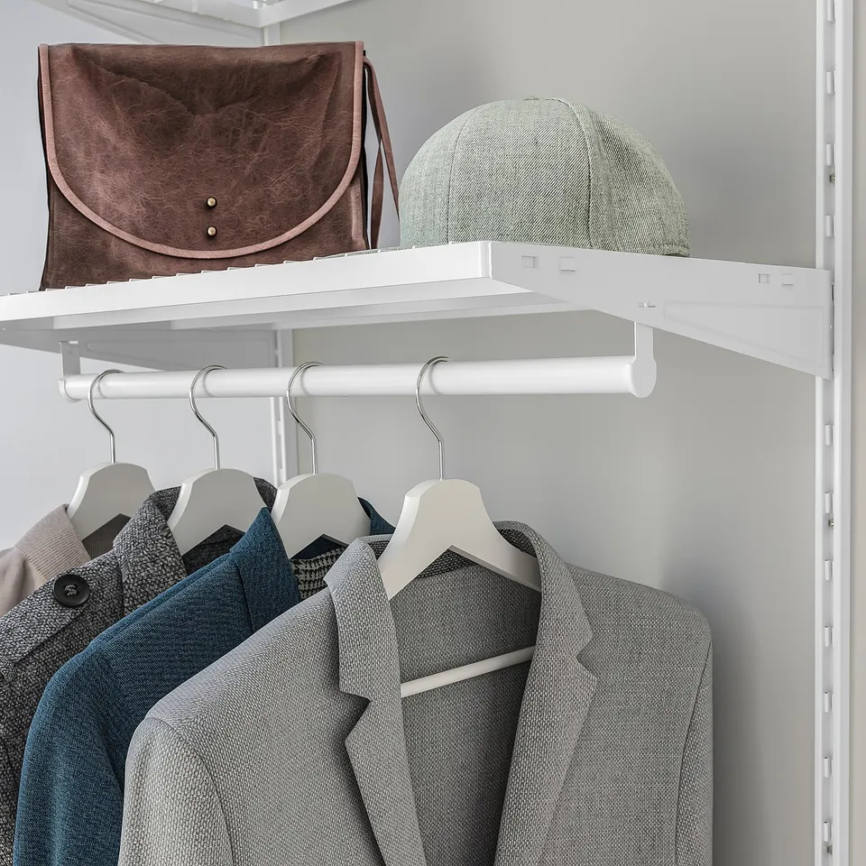 Closet shelf holding brown bag and grey hat above hanging jackets.