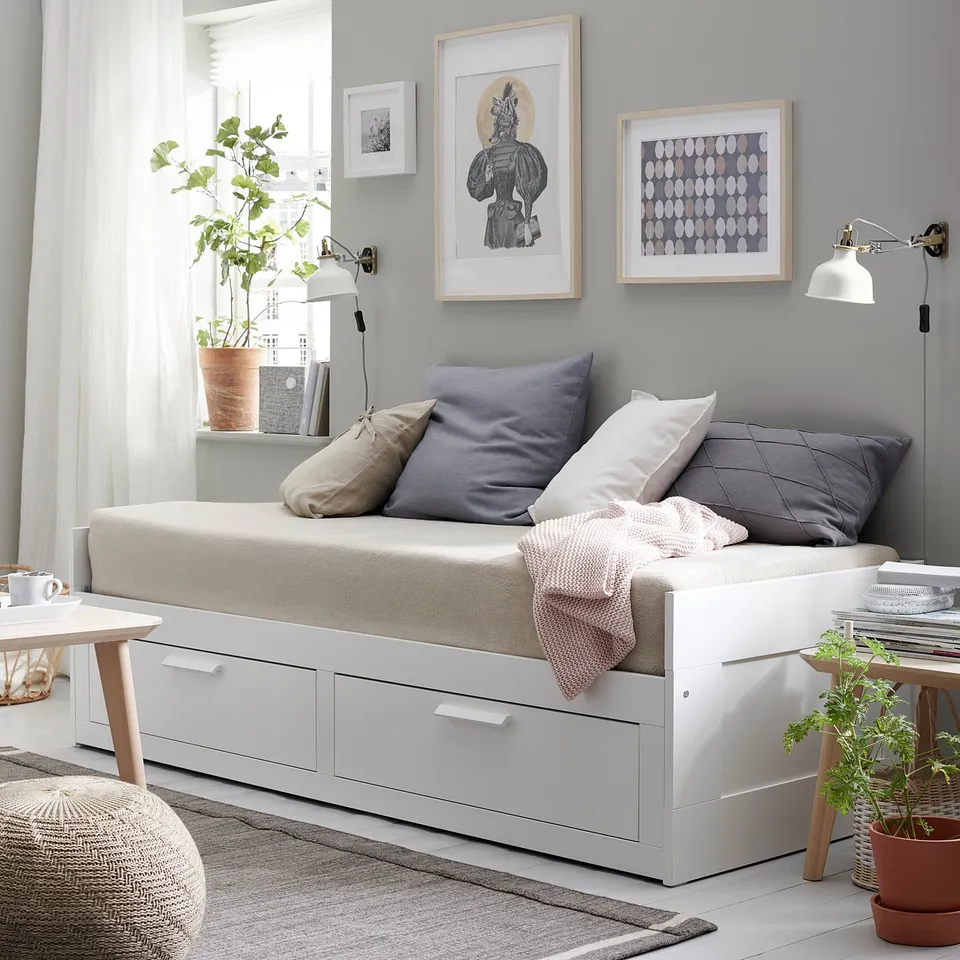 Cosy daybed BRIMNES in white with storage drawers, soft pillows, and decorative art. Bright, minimalist bedroom with plants.