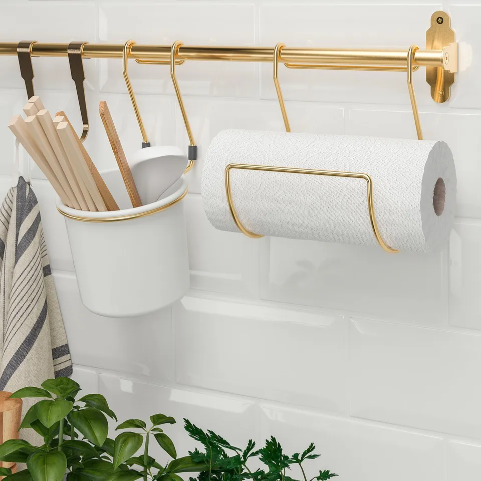 Wall-mounted kitchen organiser with hanging hooks, holding utensil caddy and paper towel holder.