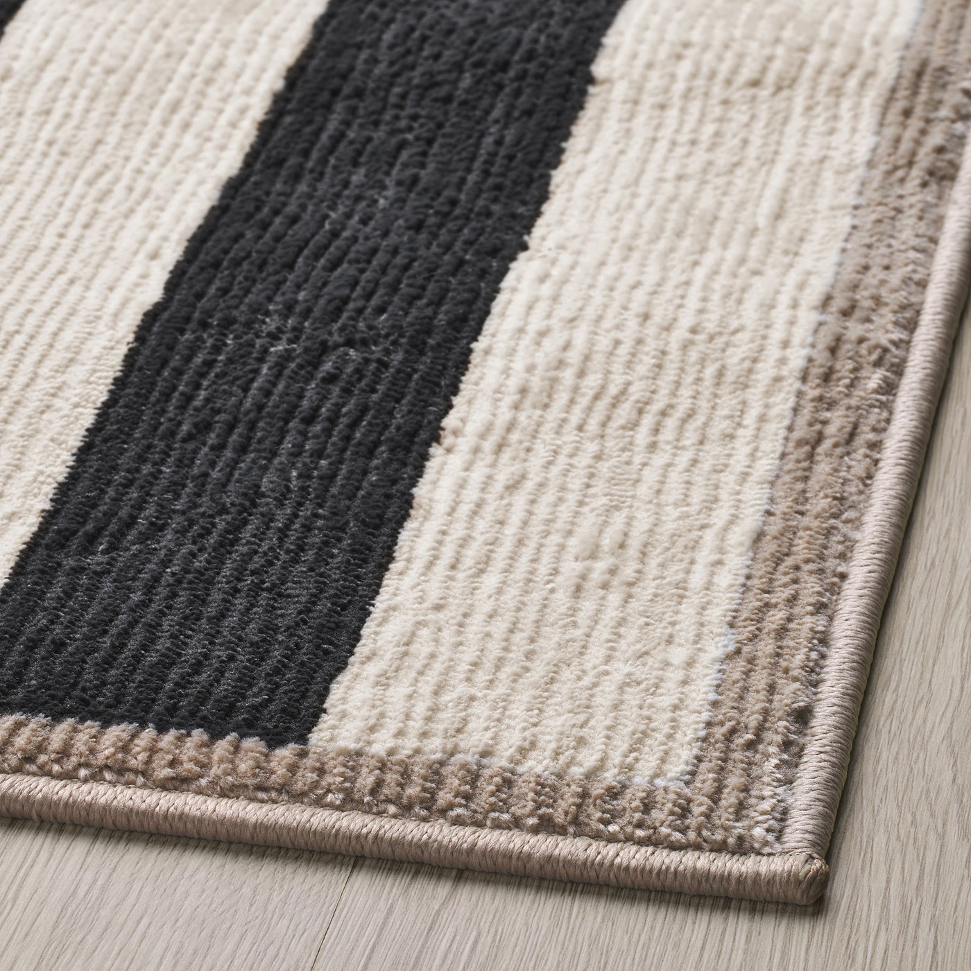 Modern horizontal striped rug with alternating black, tan, and white bands, featuring a soft texture and plush pile, situated on a wooden floor.