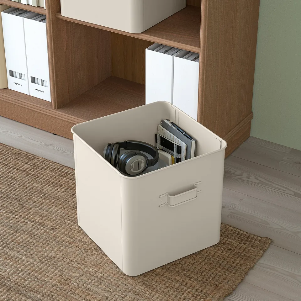 White PLOGFÅRA storage box with handle, holding headphones and papers, perfect for organising office supplies.
