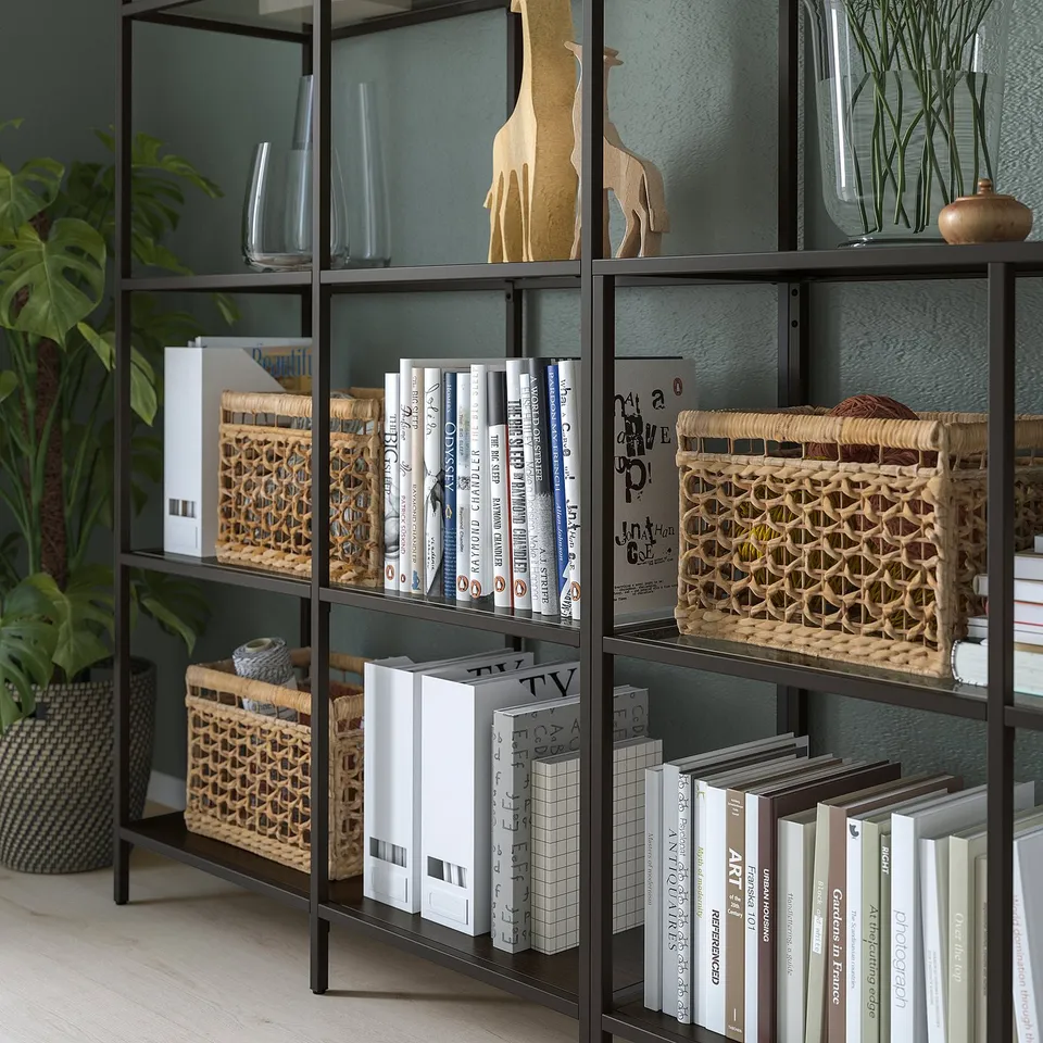 Black metal bookshelf with glass shelves holding books, baskets, vases, and a giraffe decoration.