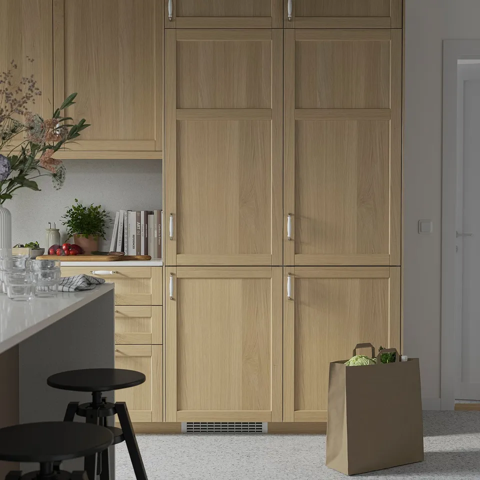 Modern kitchen with light wood cabinets, flowers, books, chair, and veggies.