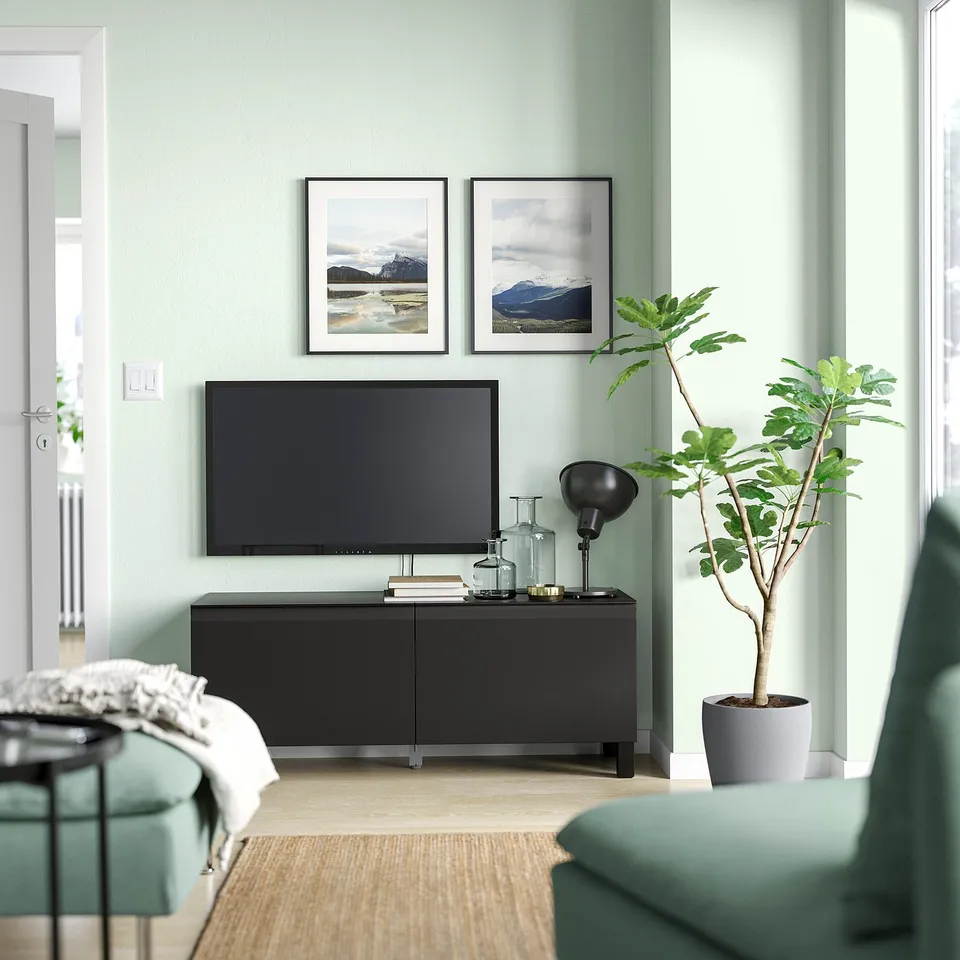 Modern living room a black BESTÅ tv stand with a flat screen, framed mountain photos, a green sofa, and a tall potted plant.