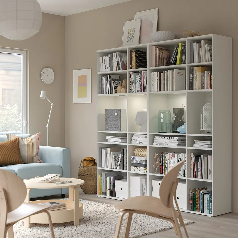 Modern living room with grey shelves, books, light blue chair, side table, and lamp.