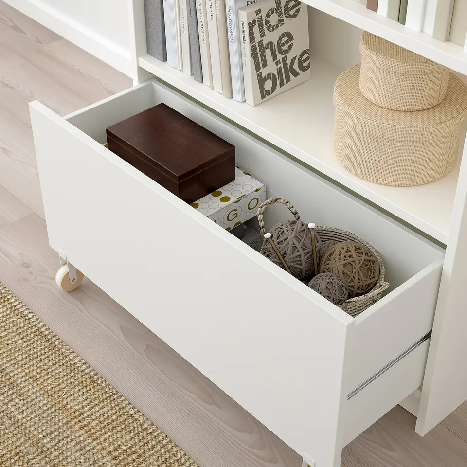 Open white BILLY drawer with castors, storing various items.