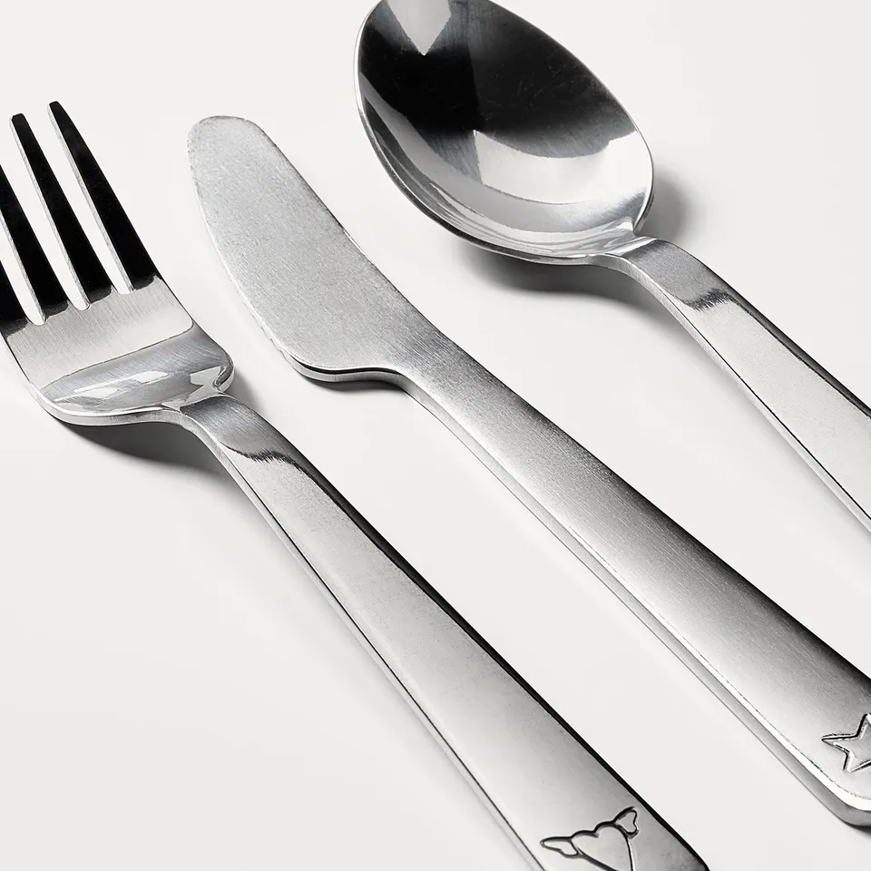 A polished stainless steel cutlery set for children, including a fork, knife, and spoon, arranged neatly on a white surface.