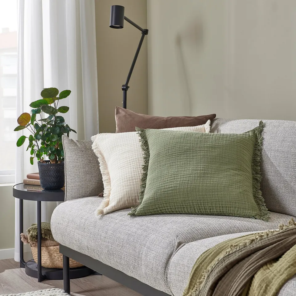 Cosy living room with grey sofa, green-white pillows, and a plant.