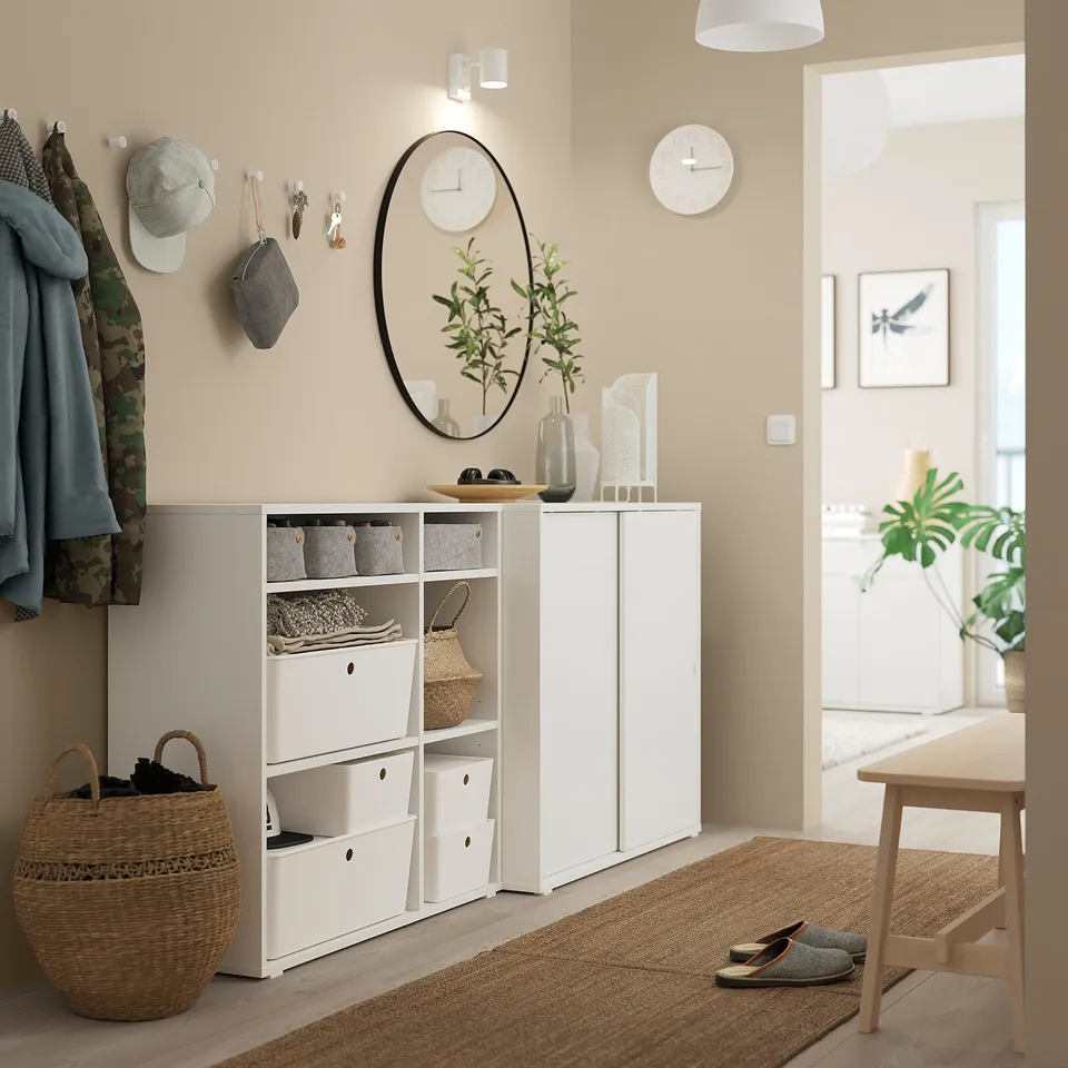 Cosy entryway with white IKEA VIHALS storage unit, hanging coats, and a round mirror against beige wall.