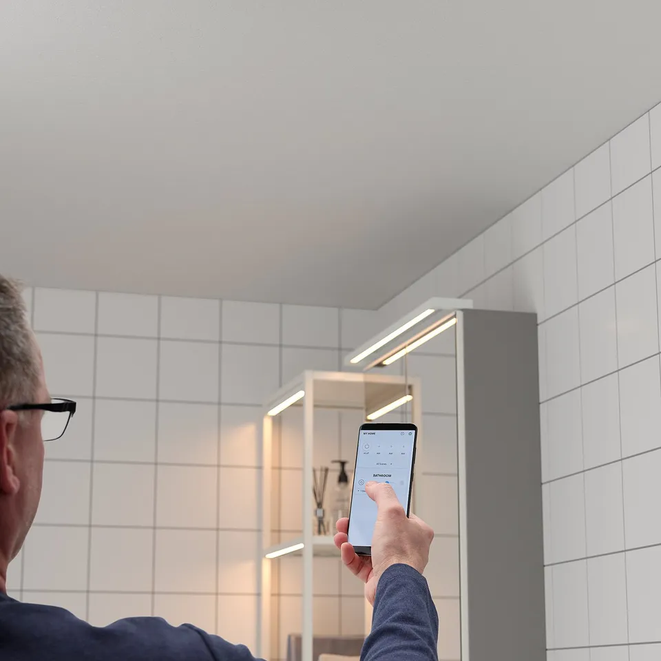 Person adjusting smart bathroom light via phone app, under-cabinet led lights.