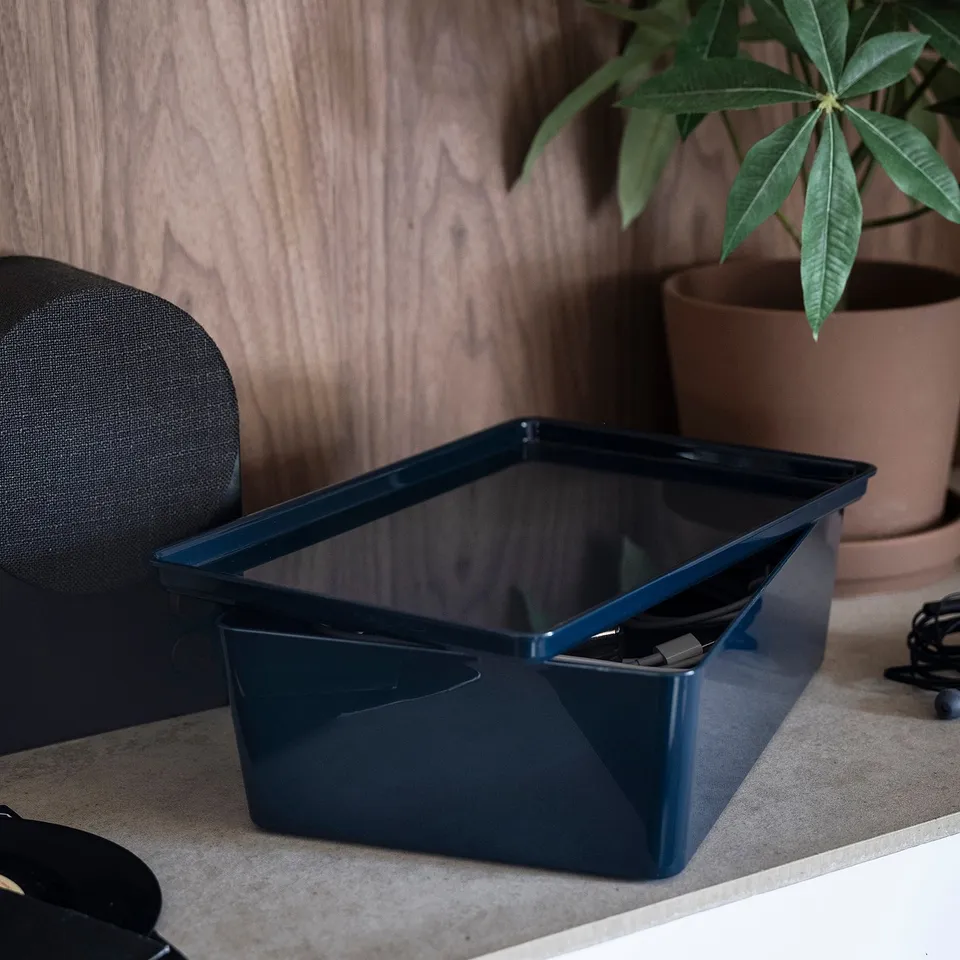 Dark blue plastic storage box on a desk holding electronic accessories. Part of the KUGGIS series for organising desk items.