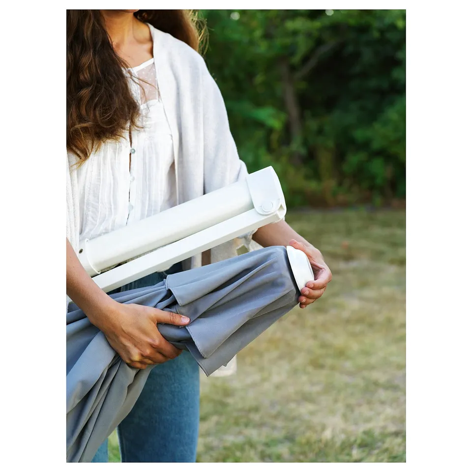 Person holding HÖGÖN parasol with grey fabric, adjusting it.
