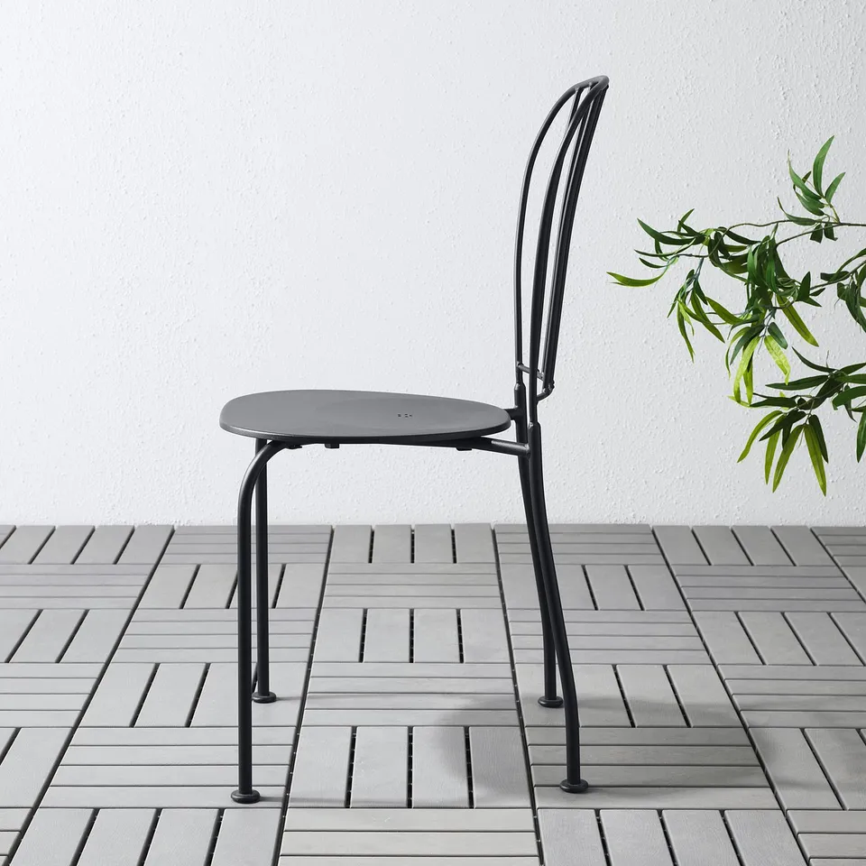 Black metal chair with round seat on tiled floor. Drain hole for easy cleaning.