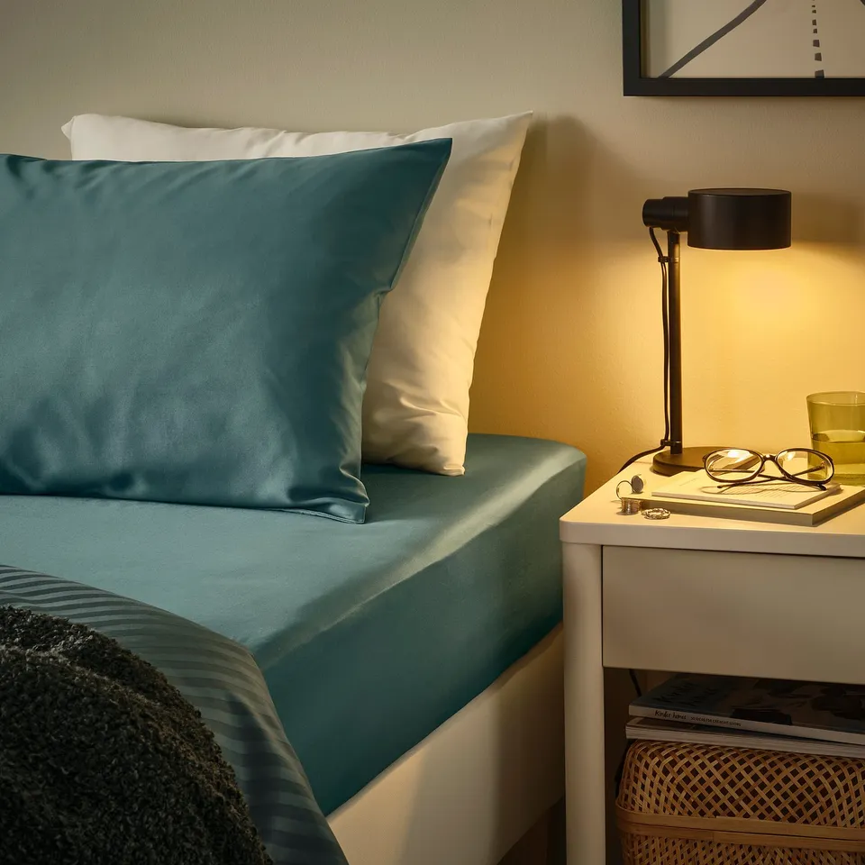 Cosy bedroom corner with teal bedding, bedside table, lamp, and decor.