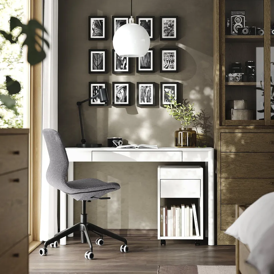 Modern home office with white TONSTAD desk, grey chair, wall art, and wooden cabinet.