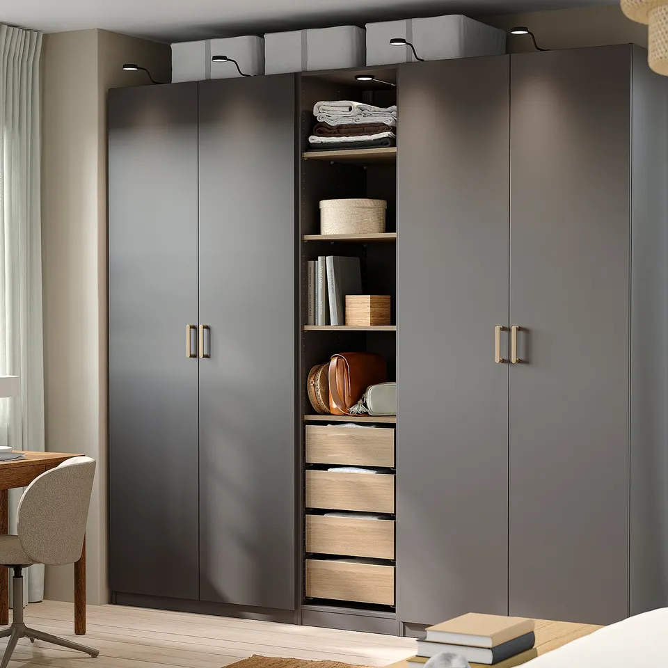 Modern grey closet with gold handles, wooden drawers, and baskets. Next to a light wooden chair and table with a red tray.