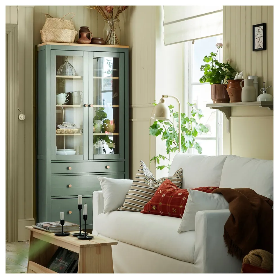 Elegant living room with green HEMNES cabinet, white sofa, red pillows, plants, and lamp.