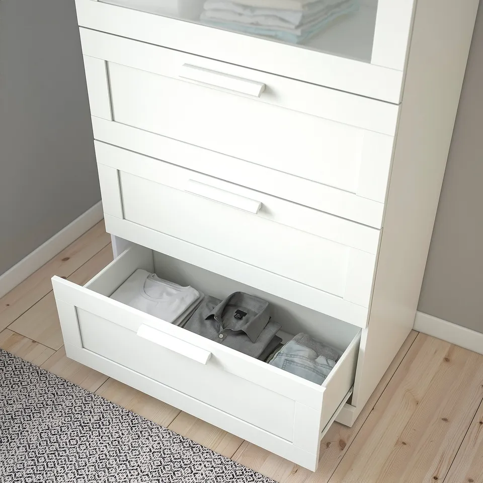 A white chest of drawers with a frosted glass top. One drawer is open, showing neatly folded clothes.